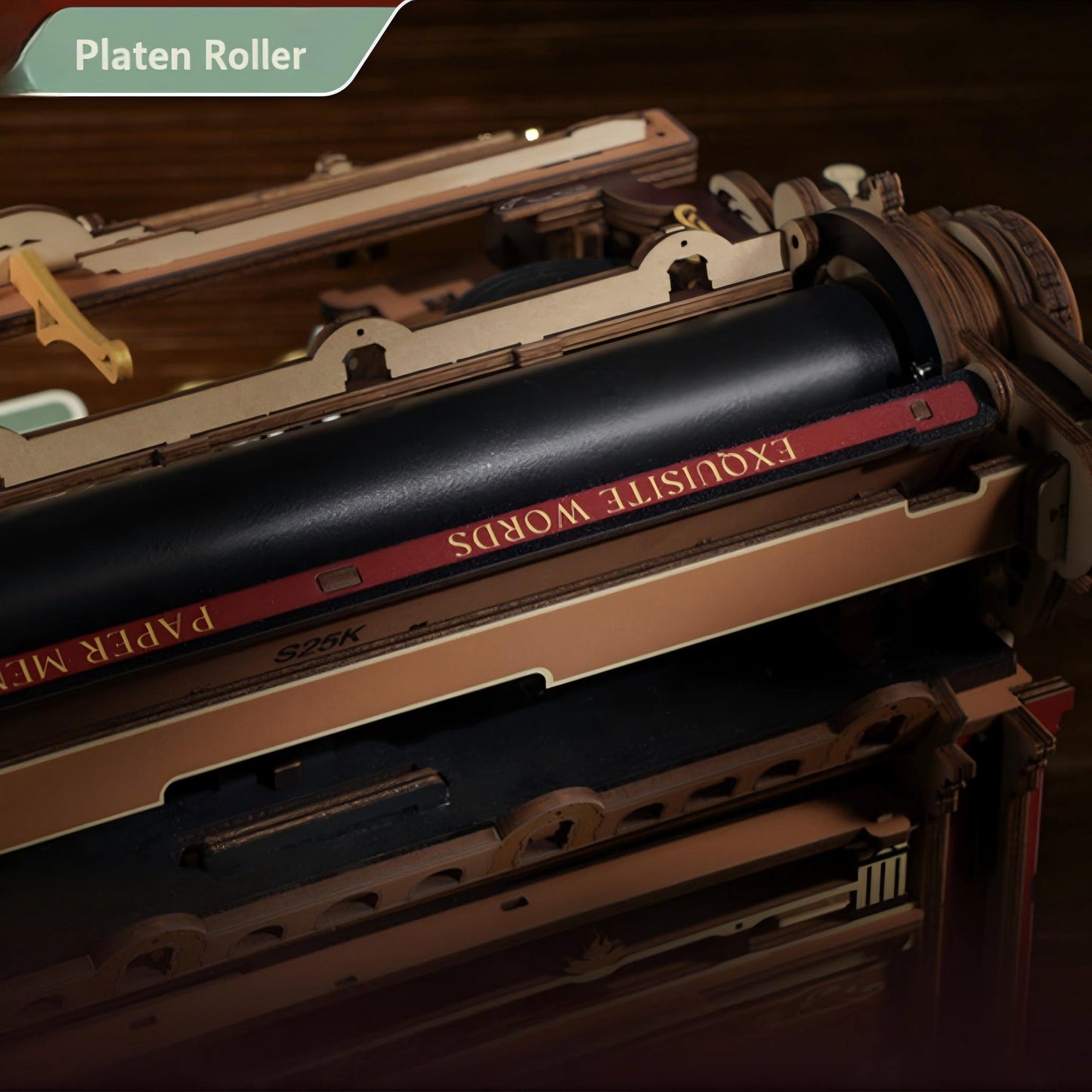 A close-up of a wooden typewriter model with a black roller printed with the words 'EXQUISITE WORDS' in gold on a red stripe, set against a dark wood background. A green banner in the top left corner reads 'Platen Roller'.