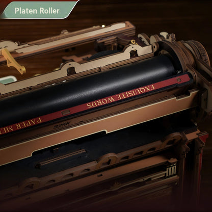 A close-up of a wooden typewriter model with a black roller printed with the words 'EXQUISITE WORDS' in gold on a red stripe, set against a dark wood background. A green banner in the top left corner reads 'Platen Roller'.