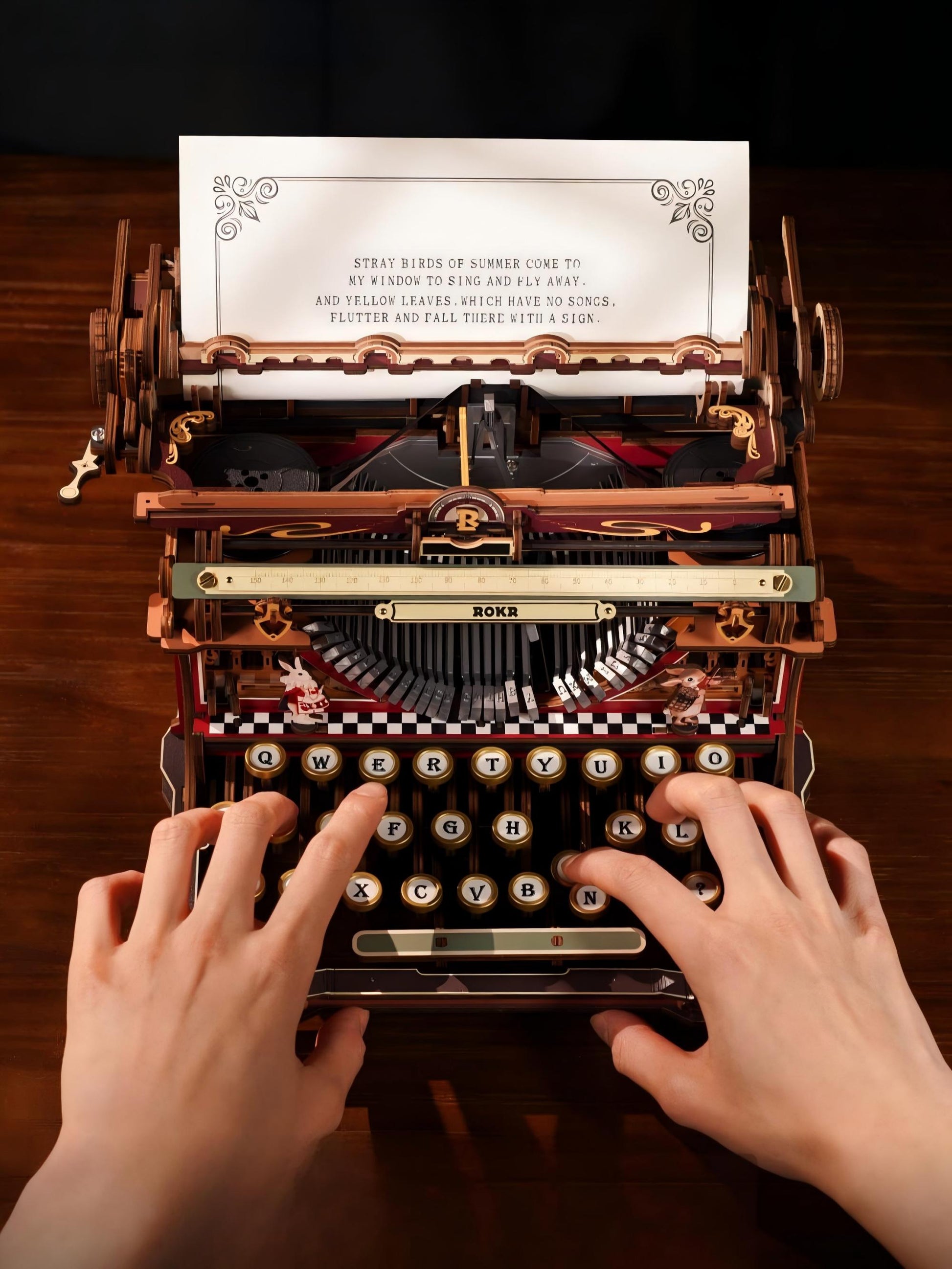 A vintage-style wooden typewriter with ornate metal details and a printed poem on the page, being used by two hands typing on a dark wood desk.